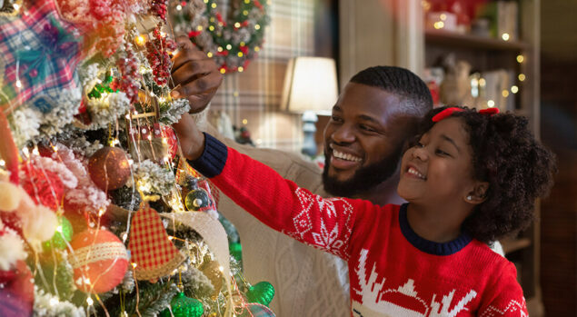 Father and daughter placing ornament on tree
